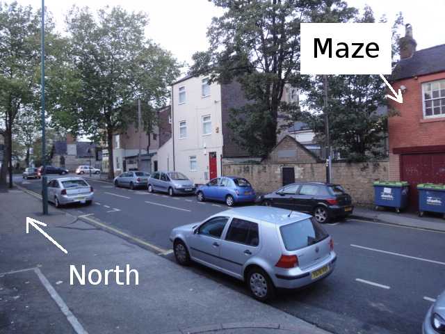 Photo: From the pavement, looking along and across a road, going off into the distance on your left. The direction along the road to the left is labelled "North". There are no parking spaces available. The Maze building is across the road, mostly not in the photo.