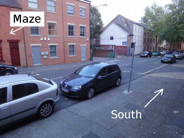 Photo: From the pavement, looking along and across a road going off into the distance on your right. The direction along the road to the right is labelled "South". There are no parking spaces available. The Maze building is across the road, mostly not in the photo.
